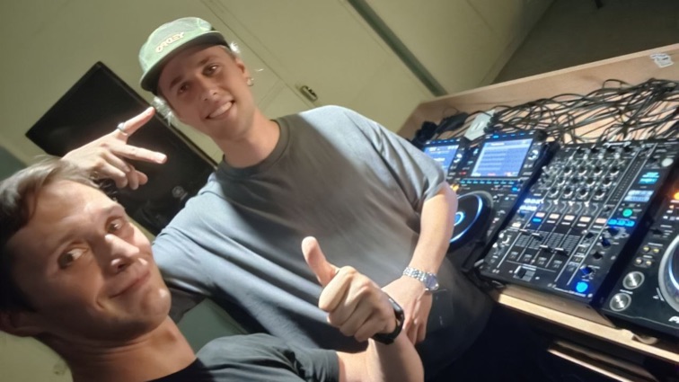 Kirill and a friend next to the DJ mixer, both smiling at the camera